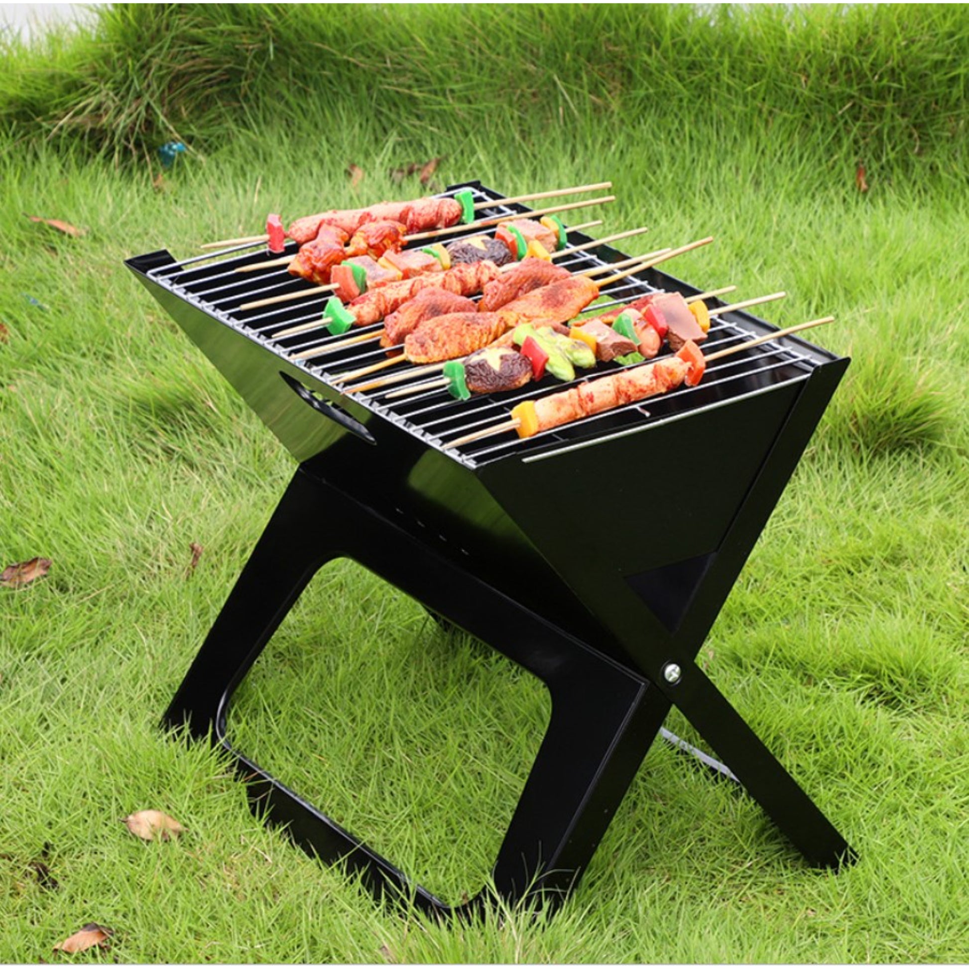 Black portable grill with skewers of food on a grassy outdoor setting
